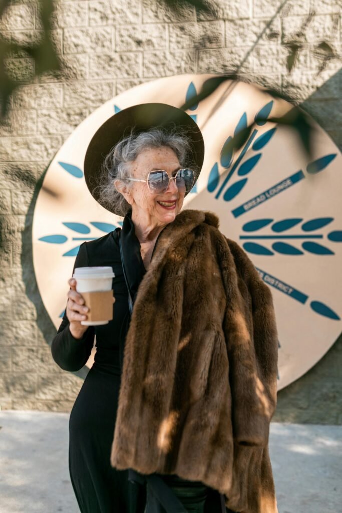 Elegant senior woman sipping coffee in a fur coat, enjoying a sunny day outdoors.