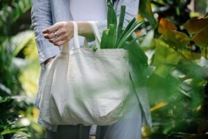 Woman carrying eco-friendly bag with green leaves in a lush garden setting.